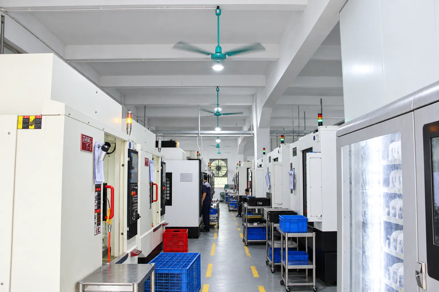 A row of CNC vertical machining centers on the shop floor with parts staged in bins between them